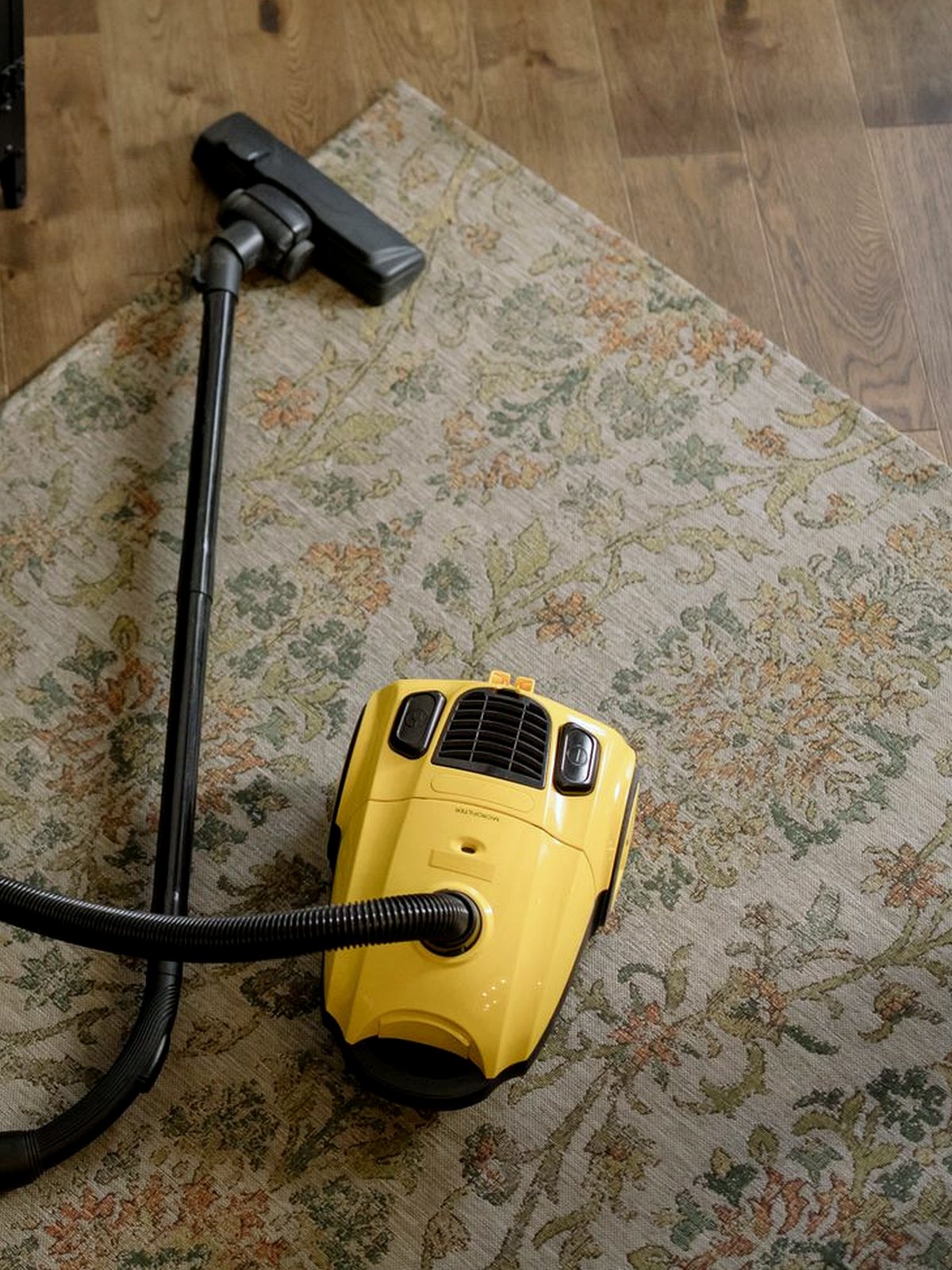 Yellow cylinder vacuum standing on a floral rug